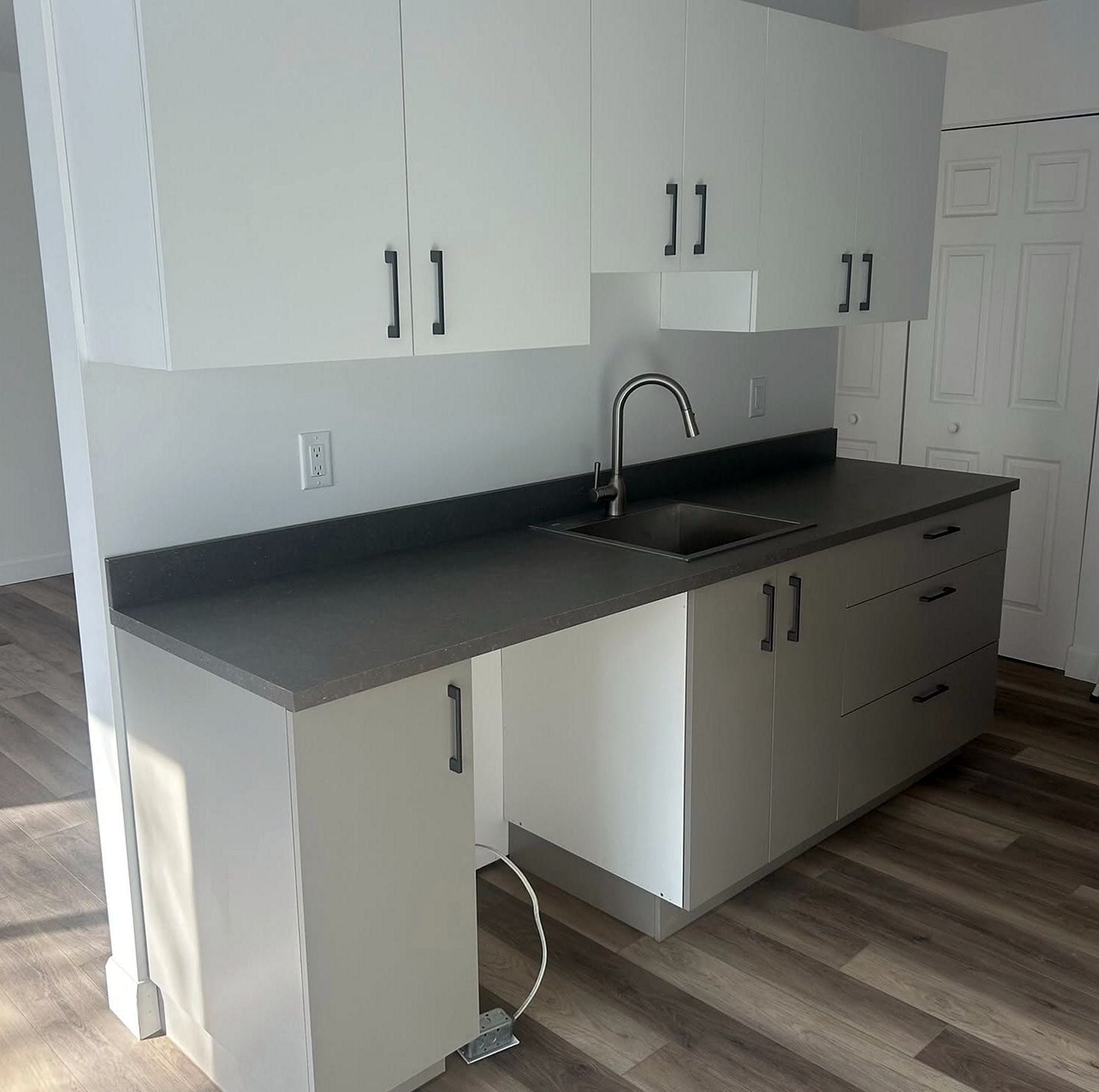 Kitchenette with white cabinets, a dark countertop and a stainless sink with a gooseneck faucet