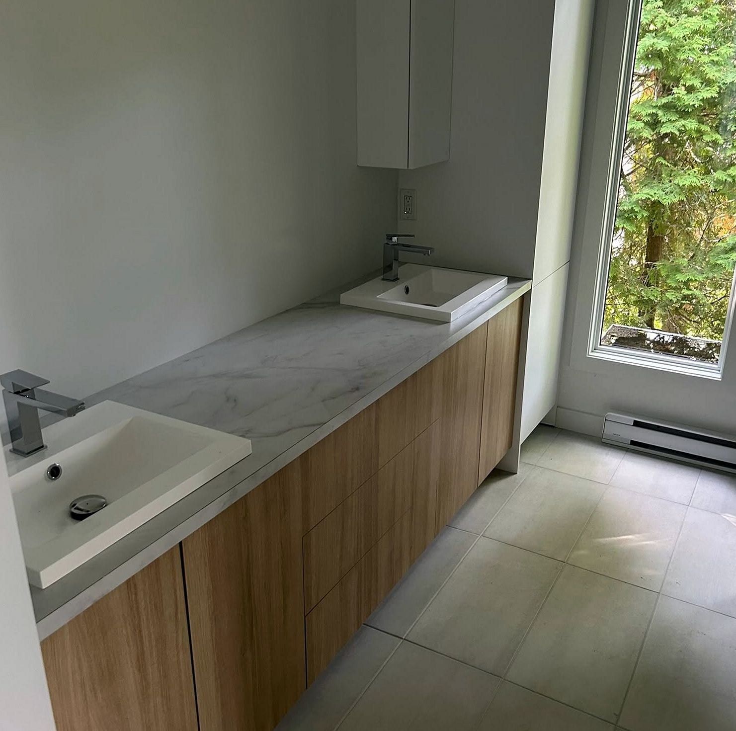 Long bathroom vanity with two square sinks and single-lever faucets beside a tall window