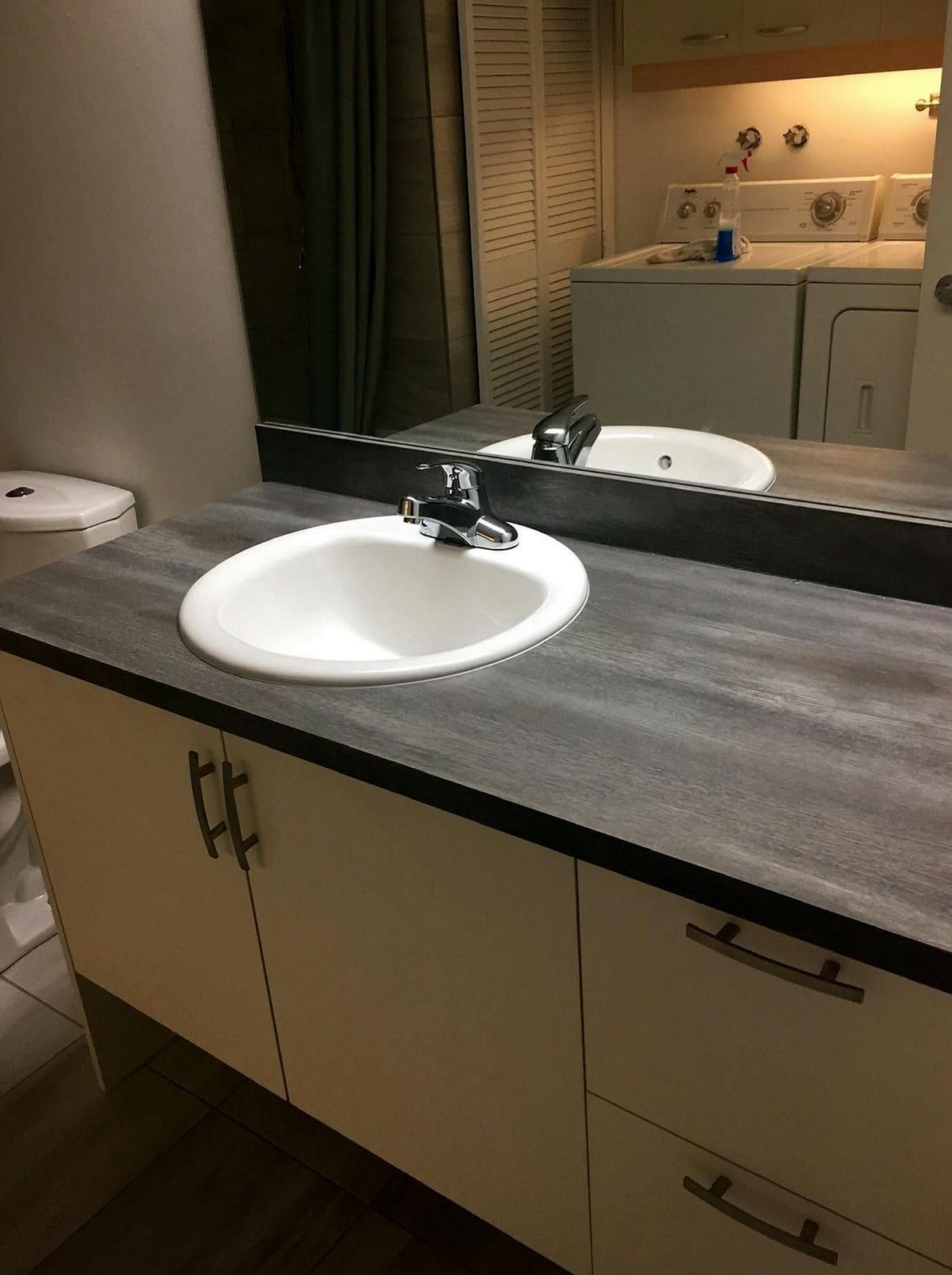 Drop-in vanity sink with a chrome faucet on a gray countertop, a laundry pair reflected in the mirror