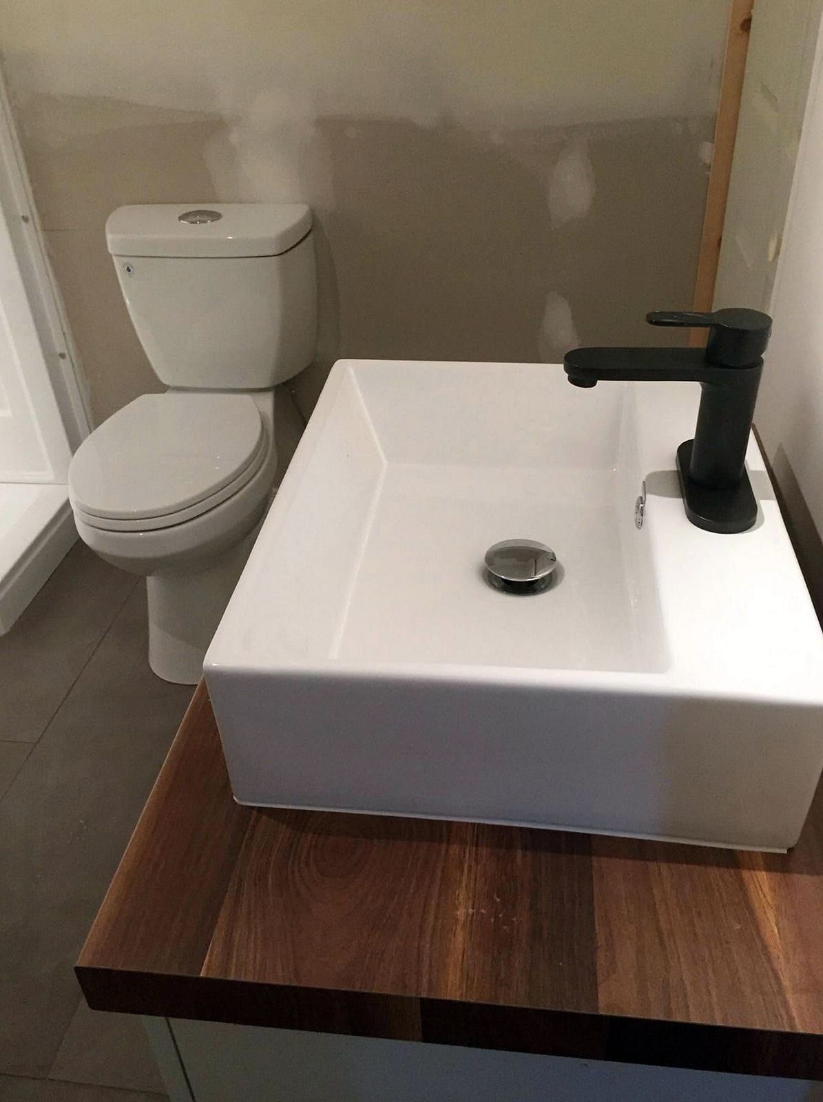 White rectangular vessel sink with a matte black faucet on a walnut countertop, a toilet behind it