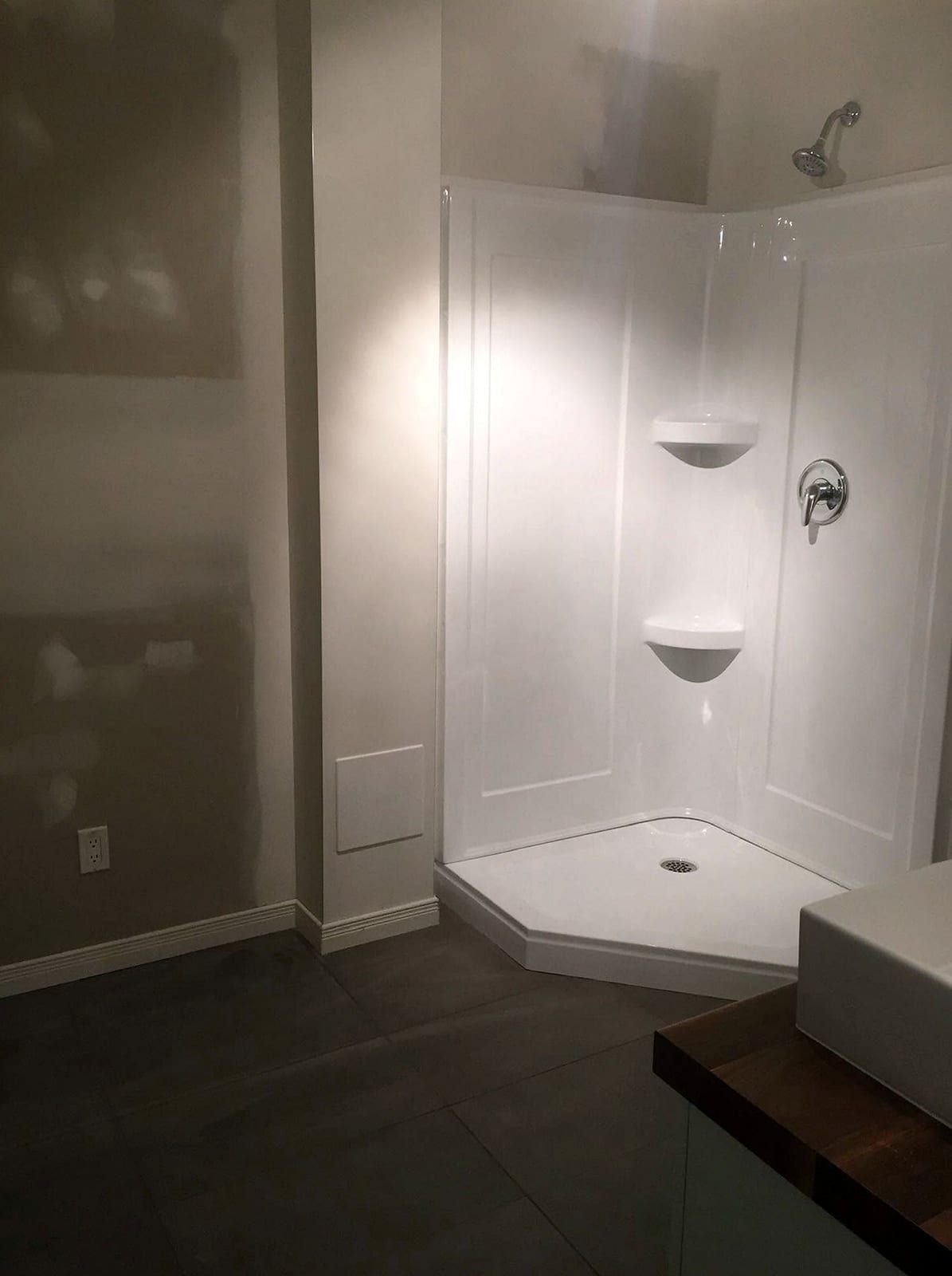 Corner shower stall with a white acrylic surround, built-in shelves and a single-handle valve