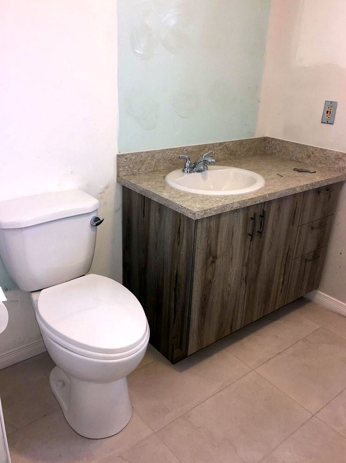 Toilet beside a wood-grain vanity with a white basin and a two-handle faucet on a stone top