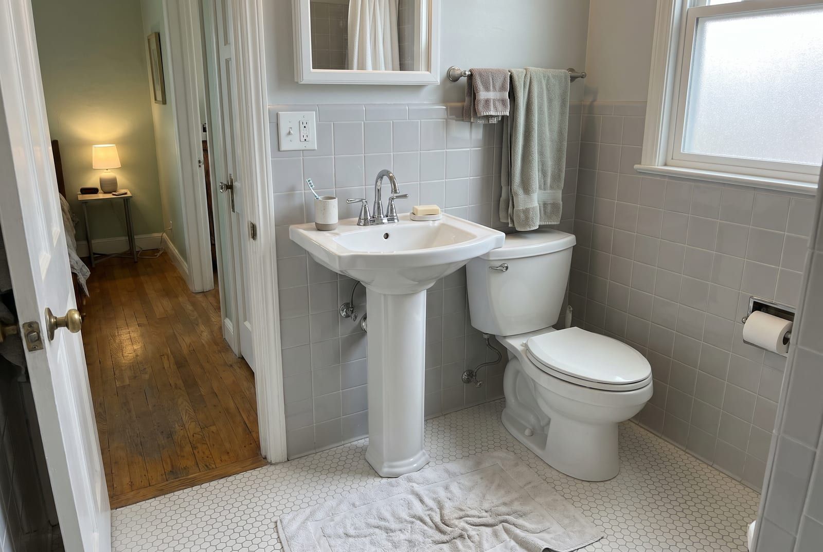 Bathroom with a pedestal sink, a toilet and pale gray ceramic tile walls