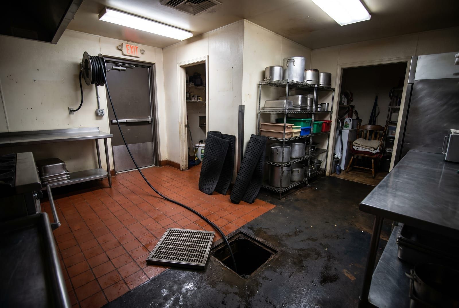 Back kitchen of a small restaurant with the floor drain grate lifted and a jetting hose run into the drain