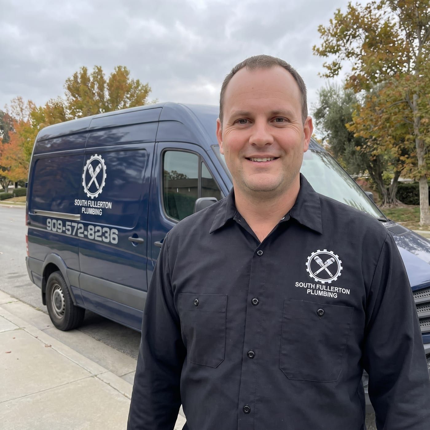 Daniel Wright in a black work shirt with the company logo, standing at the curb beside the company van on an overcast afternoon